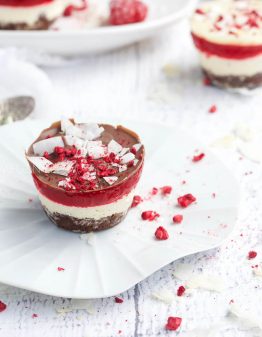 Keto Lamington Cheesecakes on white plates and a white table with crushed raspberries
