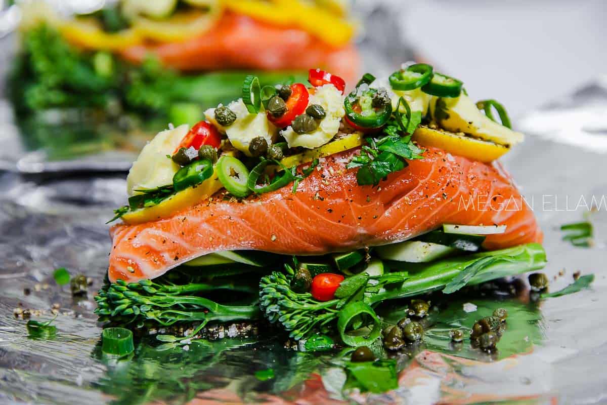 A close up of a raw salmon with vegetables and mayo on a piece of foil.