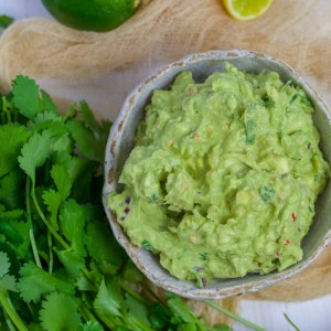 4 ingredient Guacamole in a white bowl with fresh coriander to the side.