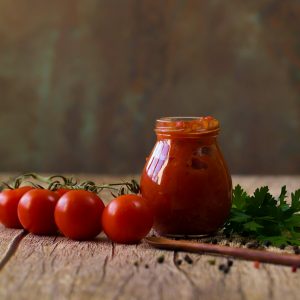 tomatoes, herbs, pepper and a jar of sauce on a wood table