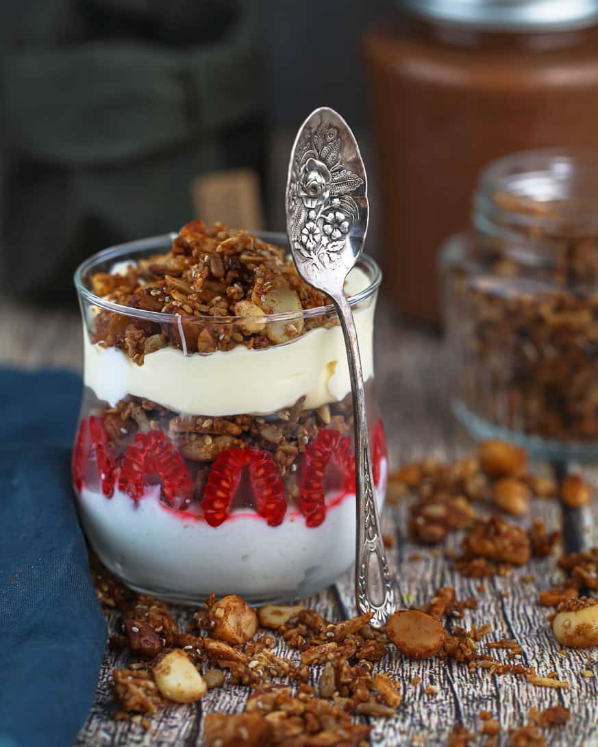 granola and cream in a glass with berries and a spoon leaning against it