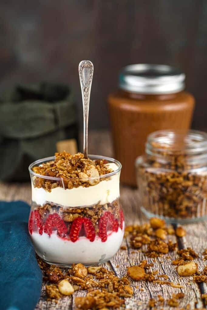 spoon in a glass of crunchy keto granola cream and raspberries