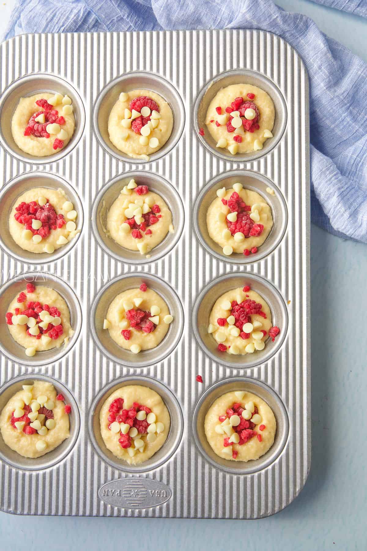 A muffin tray with raspberry muffins in the holes.