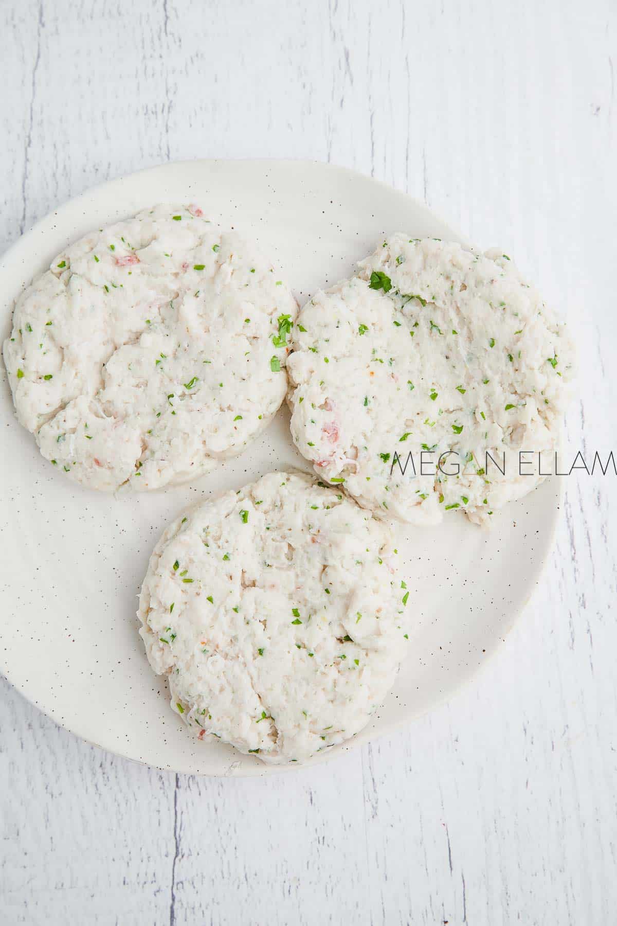 a speckled plate with three raw, uncoated fish cakes