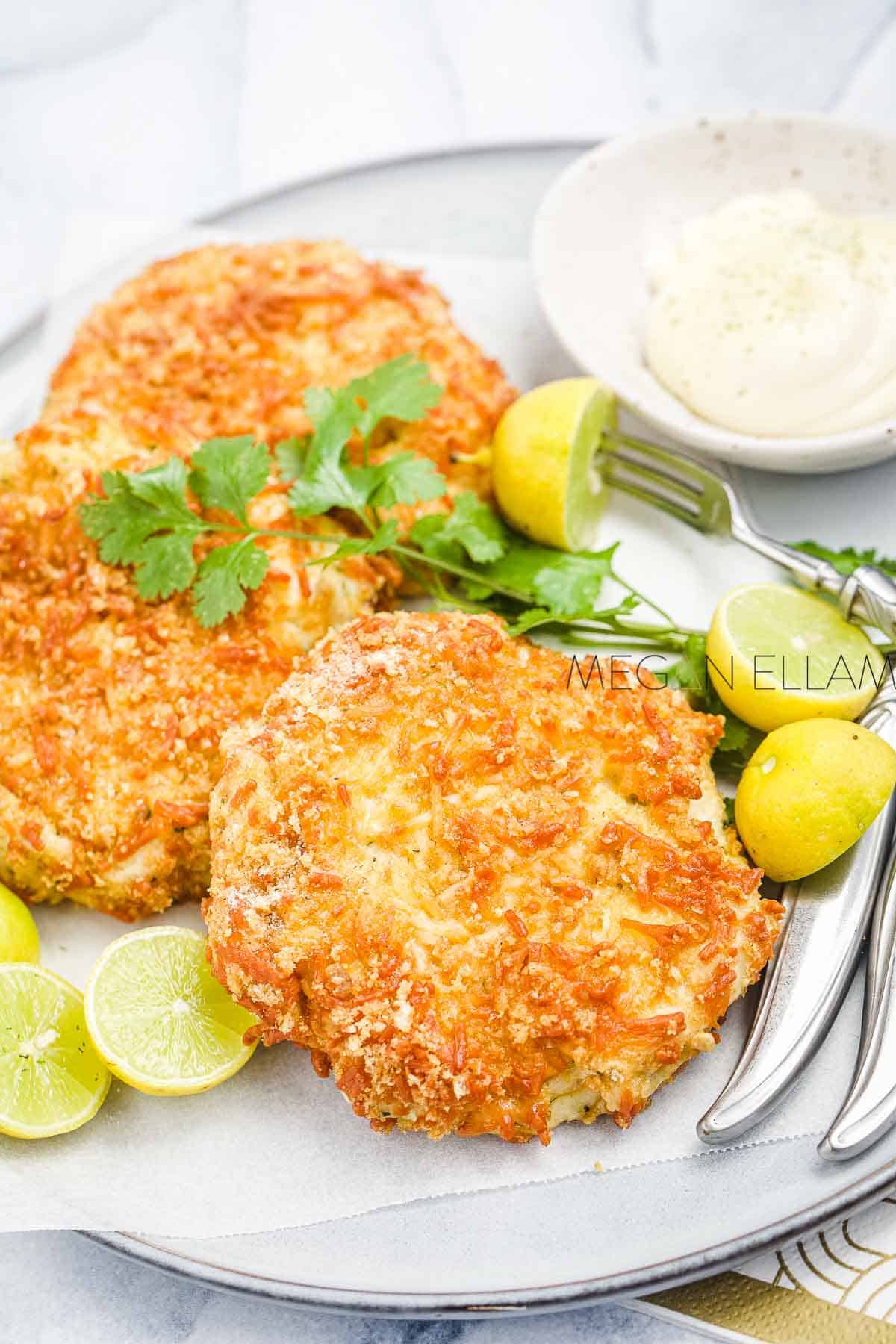Fish cakes on a plate with tartare sauce, lime halves and seafood forks