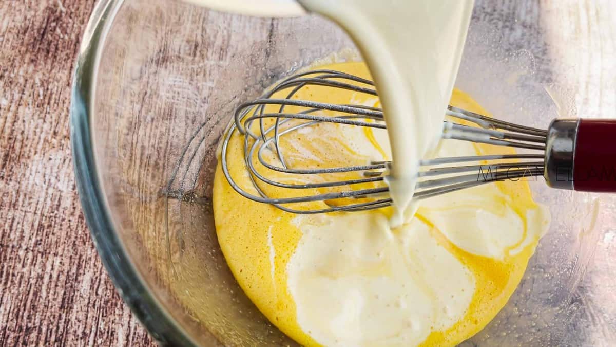 Pouring cream into whisked egg yolks.
