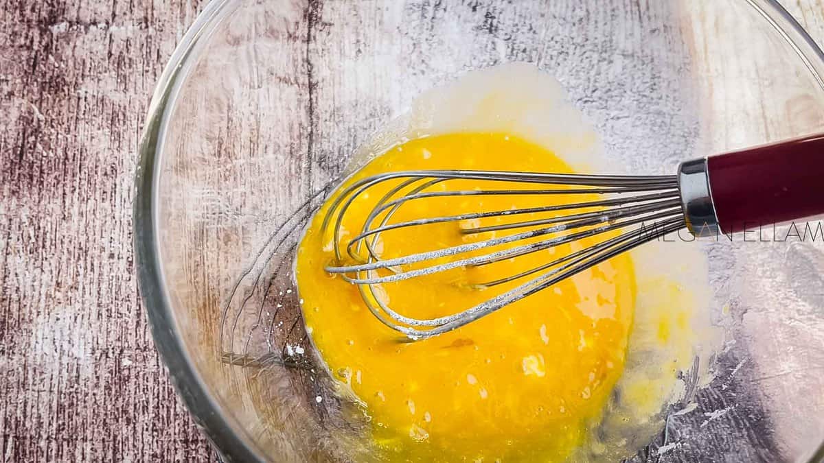 Egg yolks and sweetener in a bowl with a whisk.