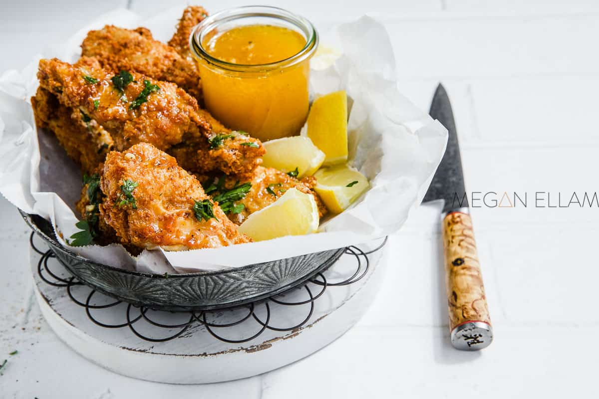 A bowl of chicken wings with a lemon butter sauce sprinkle with parsley.