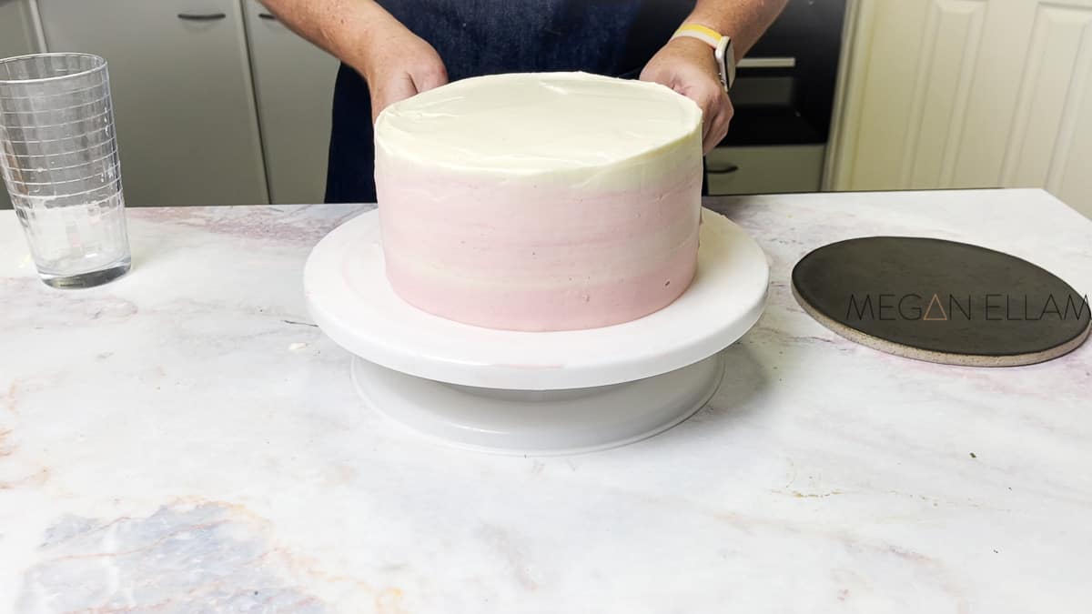 a smooth pink ombre frosted cake with a woman standing behind it.