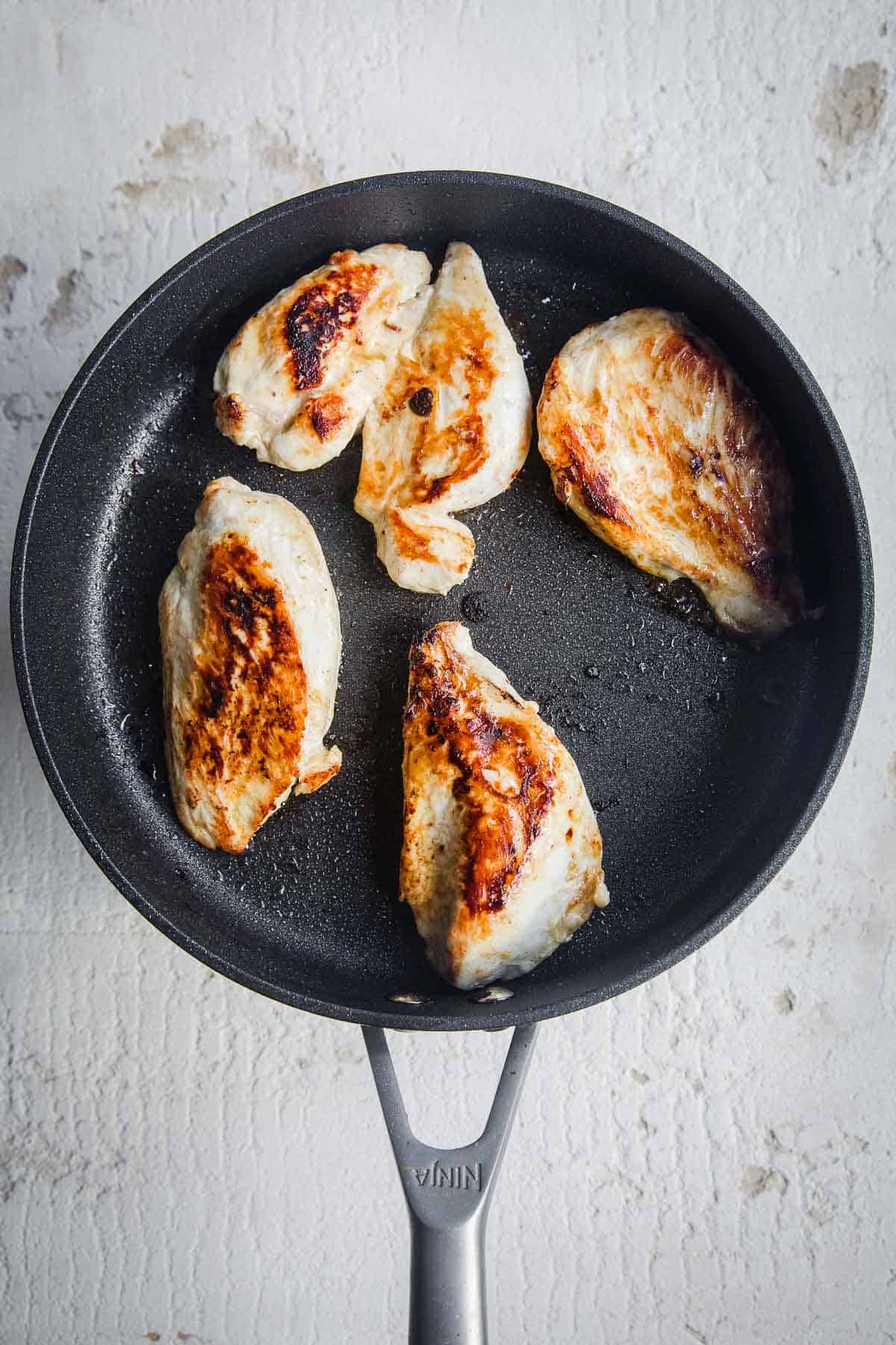 Four chicken breast in a frying pan.