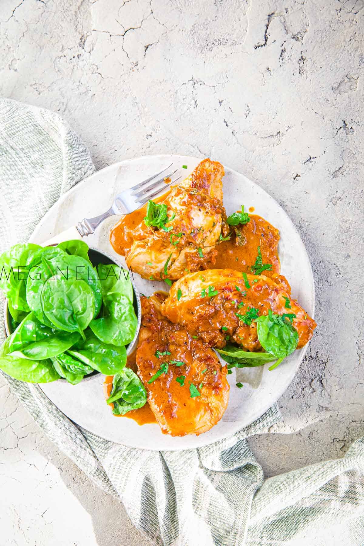 A creamy red pesto chicken and spinach leaves on a grey plate.