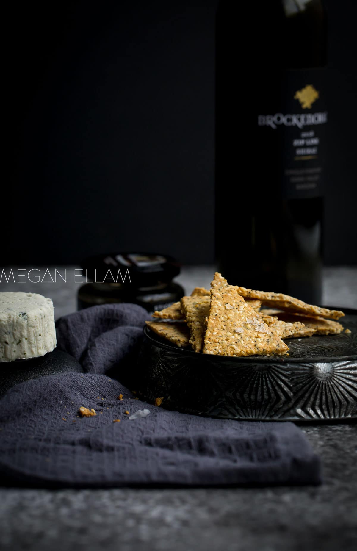 Almond Flour Crackers, a piece of Bousin cheese and a bottle of wine on a black towel.