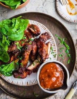 COuntry style boneless pork ribs with greens and bbq sauce on a copper plate.