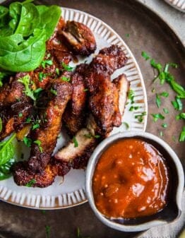 Country style boneless pork ribs on a white plate with baby spinach leaves.