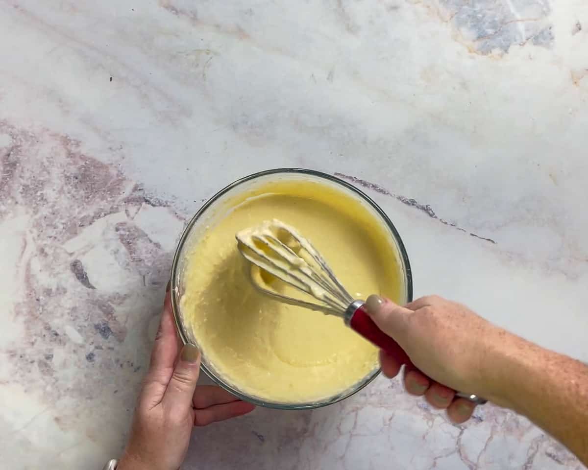 Two hands whisking a bowl of ice cream custard.