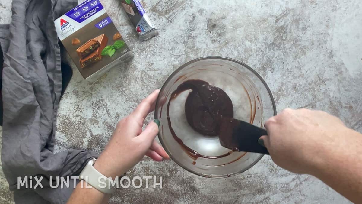 Two hands mixing chocolate ganache in a glass bowl.