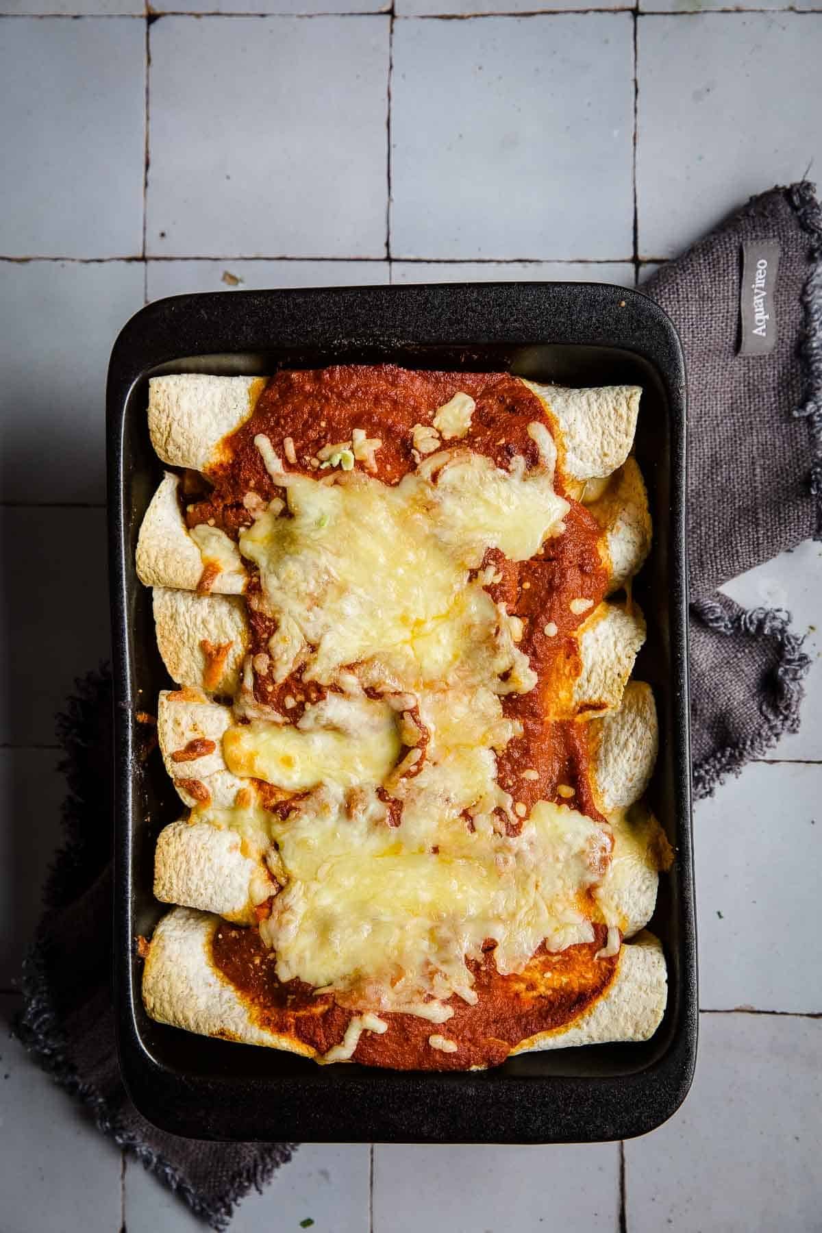 Keto Chicken Enchiladas in a black cast iron baking tray with cheese and sauce on top.