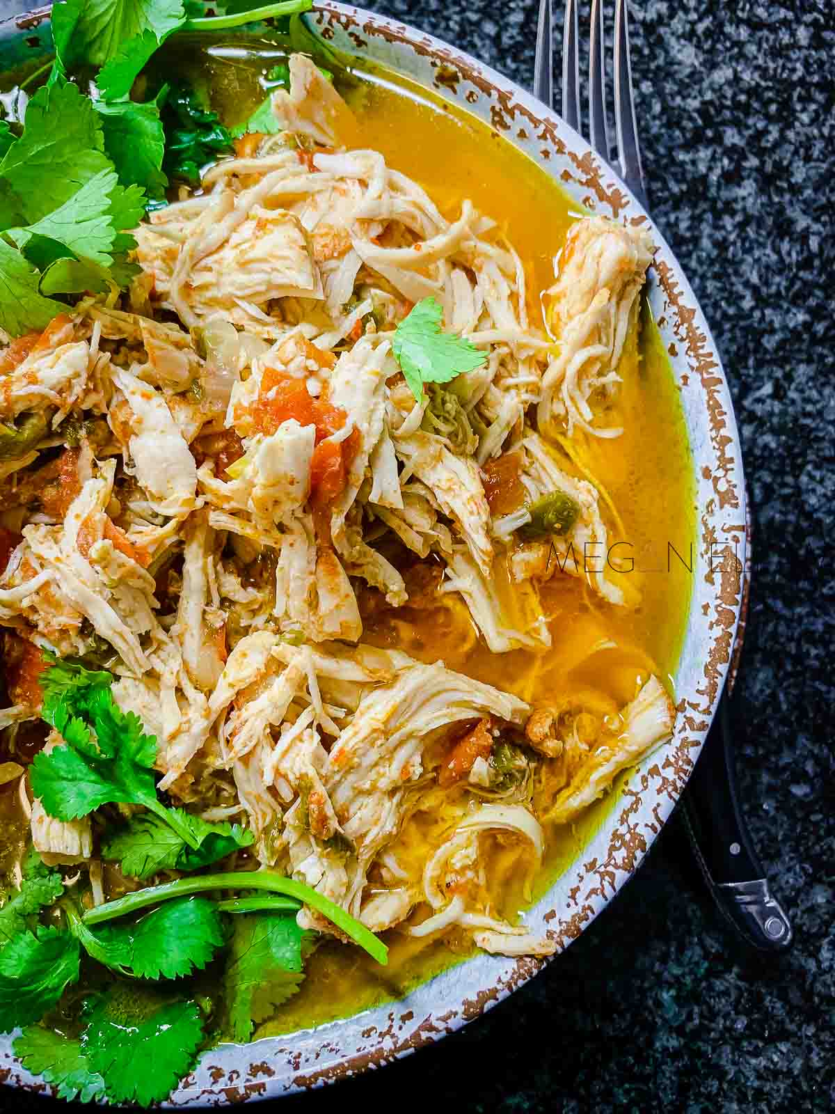 A close up of shredded chicken with fresh coriander leaves on top.