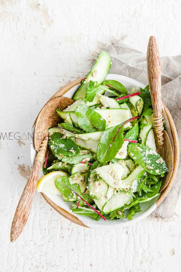 A zucchini salad with leafy green in a bowl with salad claws.