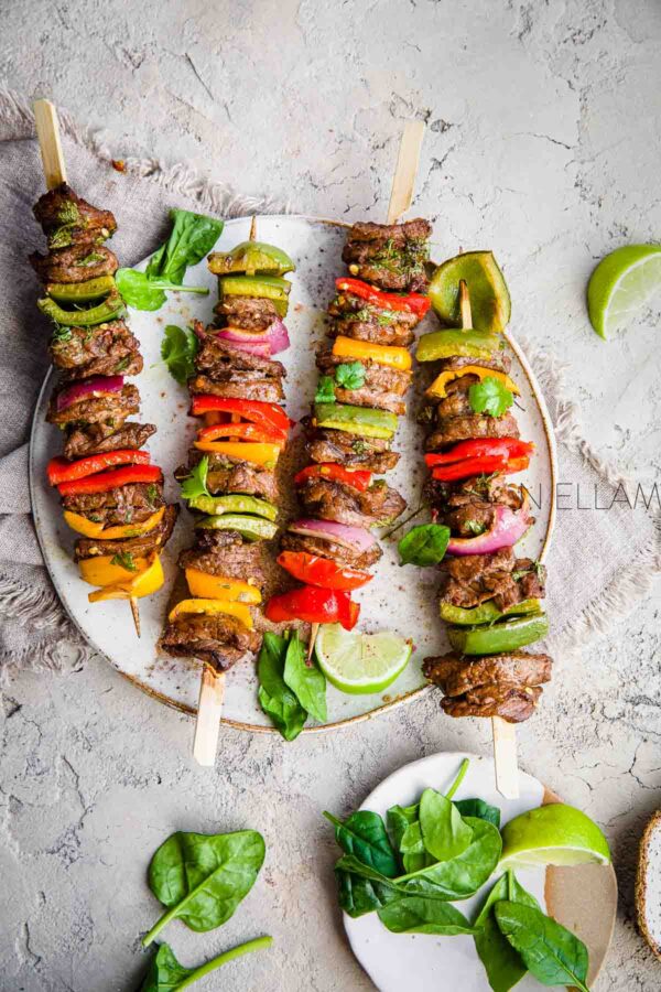 4 beef and vegetable kebabs on a greyish plate with spinach leaves.