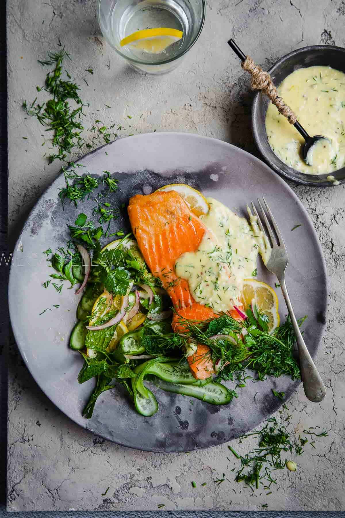 Salmon on a grey plate with a green salad and garlic sauce to the right.