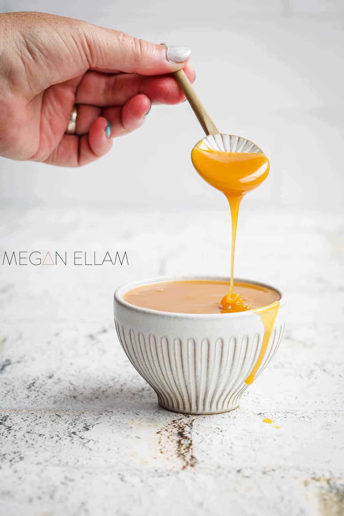 Sugar free caramel syrup being drizzled off a spoon by a womans hand.