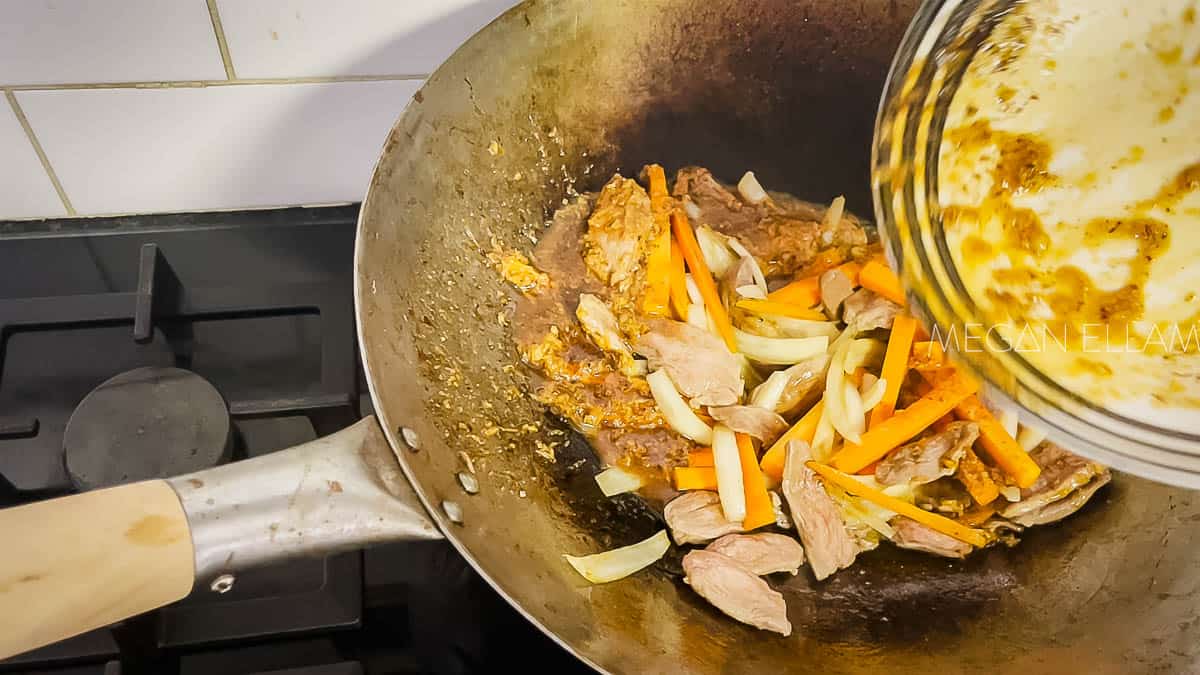 Duck and vegetables in a wok with sauce getting poured in.