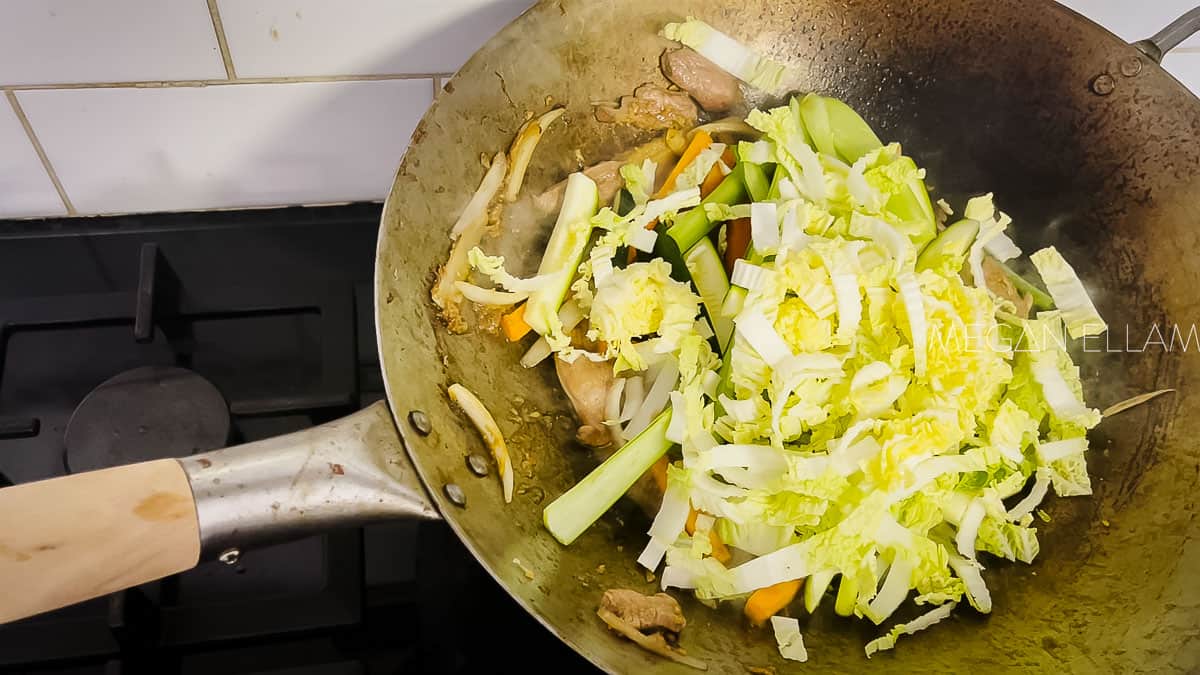 A wok with meat and loads of Chinese cabbage in it.
