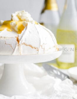 A sugar free keto pavlova on a white cake stand and topped with cream and passionfruit curd.