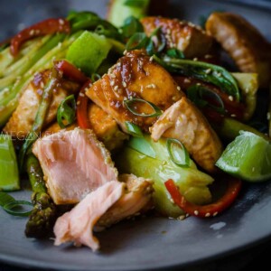 A salmon and vegetable stir fry on a grey plate.
