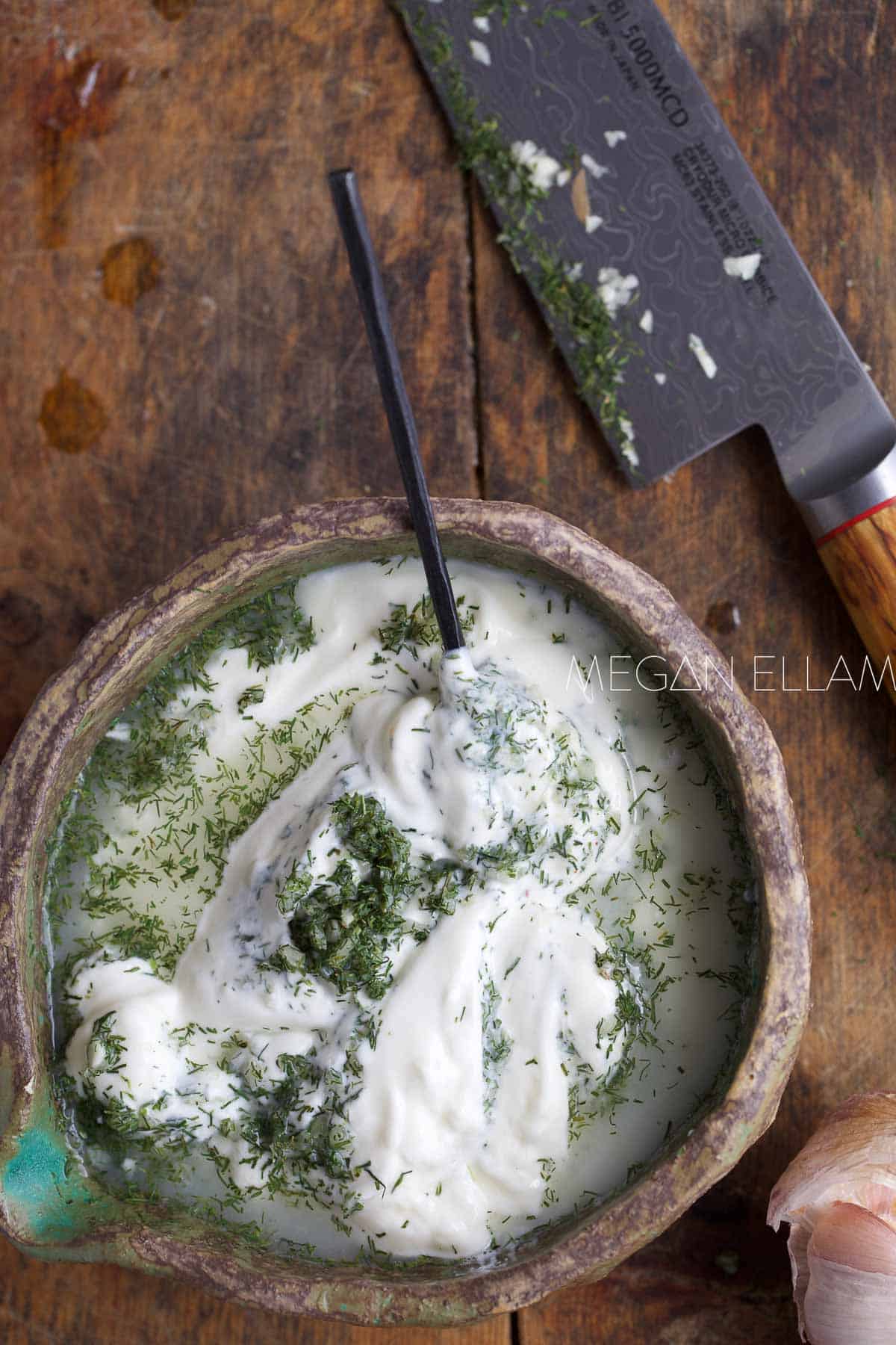 Yogurt with dill and onion in a bowl with a black spoon.