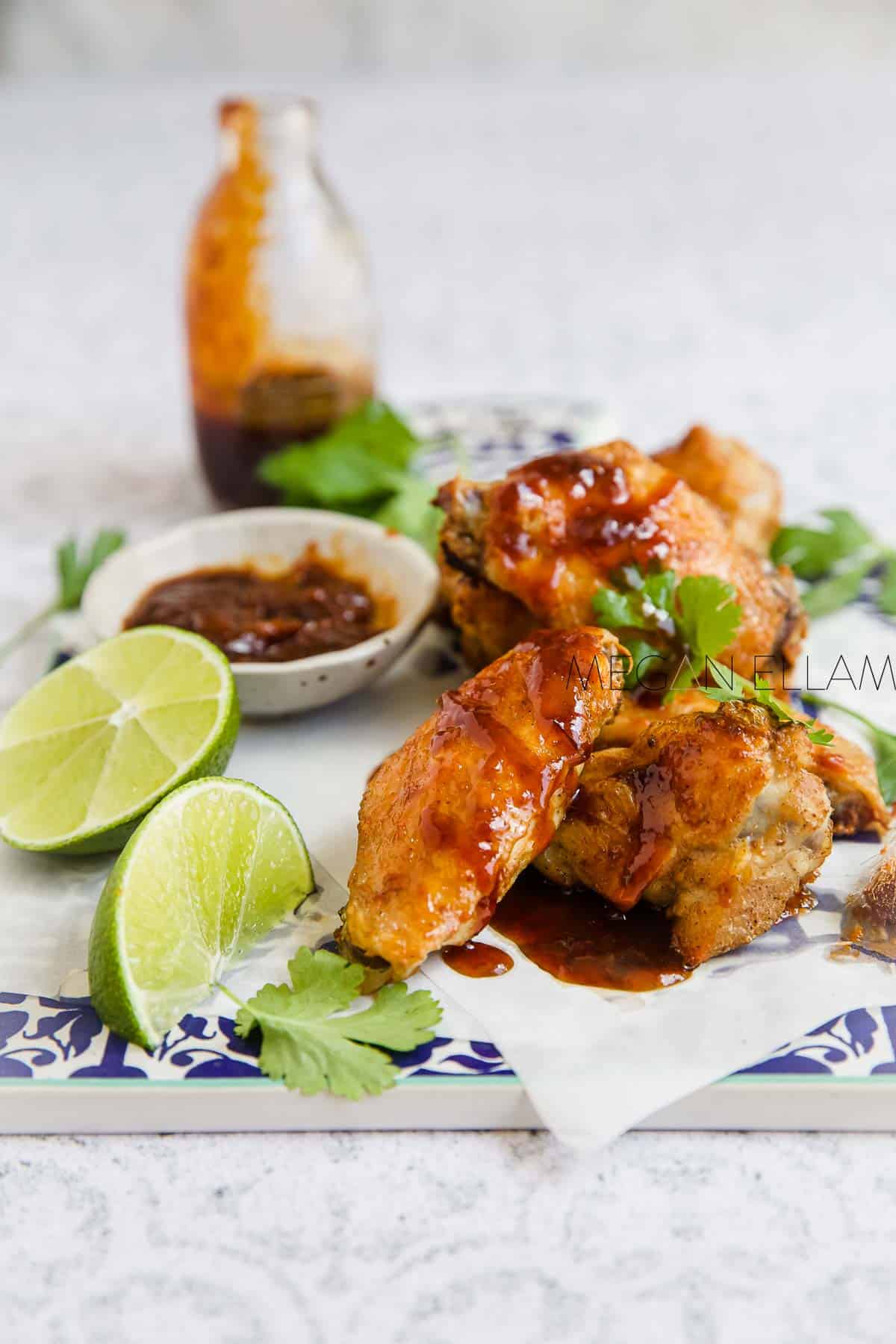 Crispy chicken wings with sauce and lime wedges on a white background.