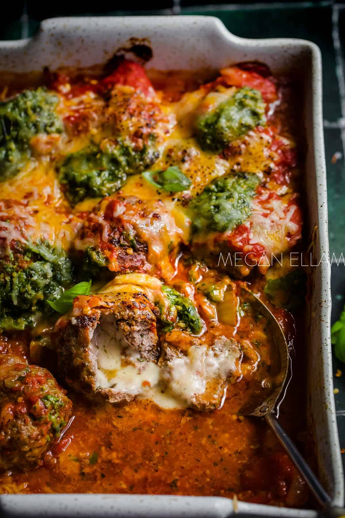 Cheese filled meatballs in a baking dish covered in tomato sauce.