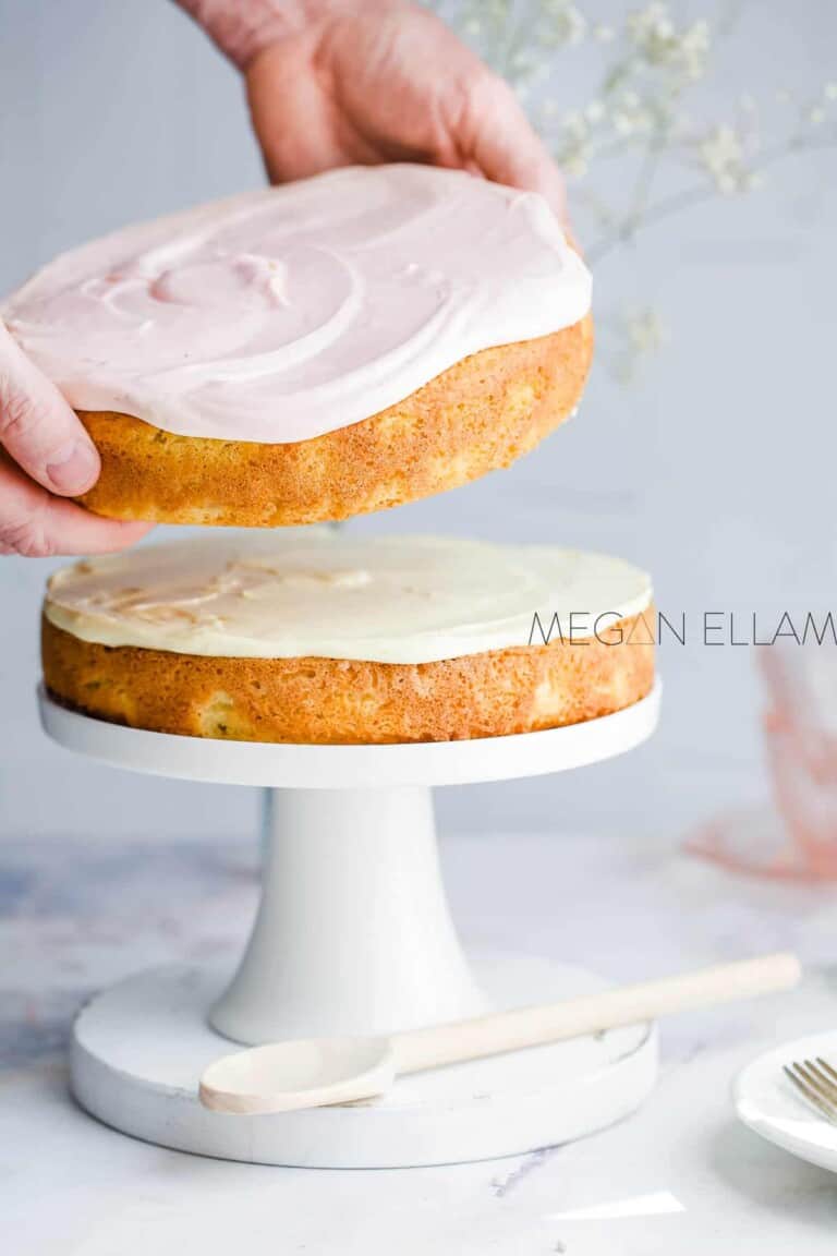A man placing a pink iced keto yellow cake on top of another one.