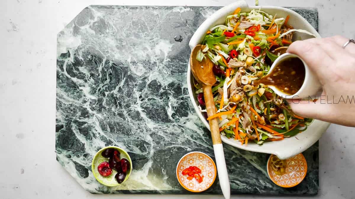 A tossed Chinese duck salad in a white bowl on a marble backdrop.