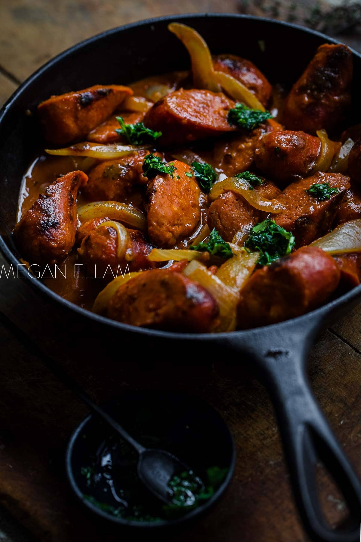 A close up of sausages in a rich curry sauce in a black pan.