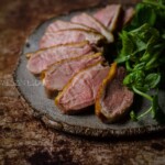 Sous Vide Duck Breast on a brown and grey plate with greens to the side.