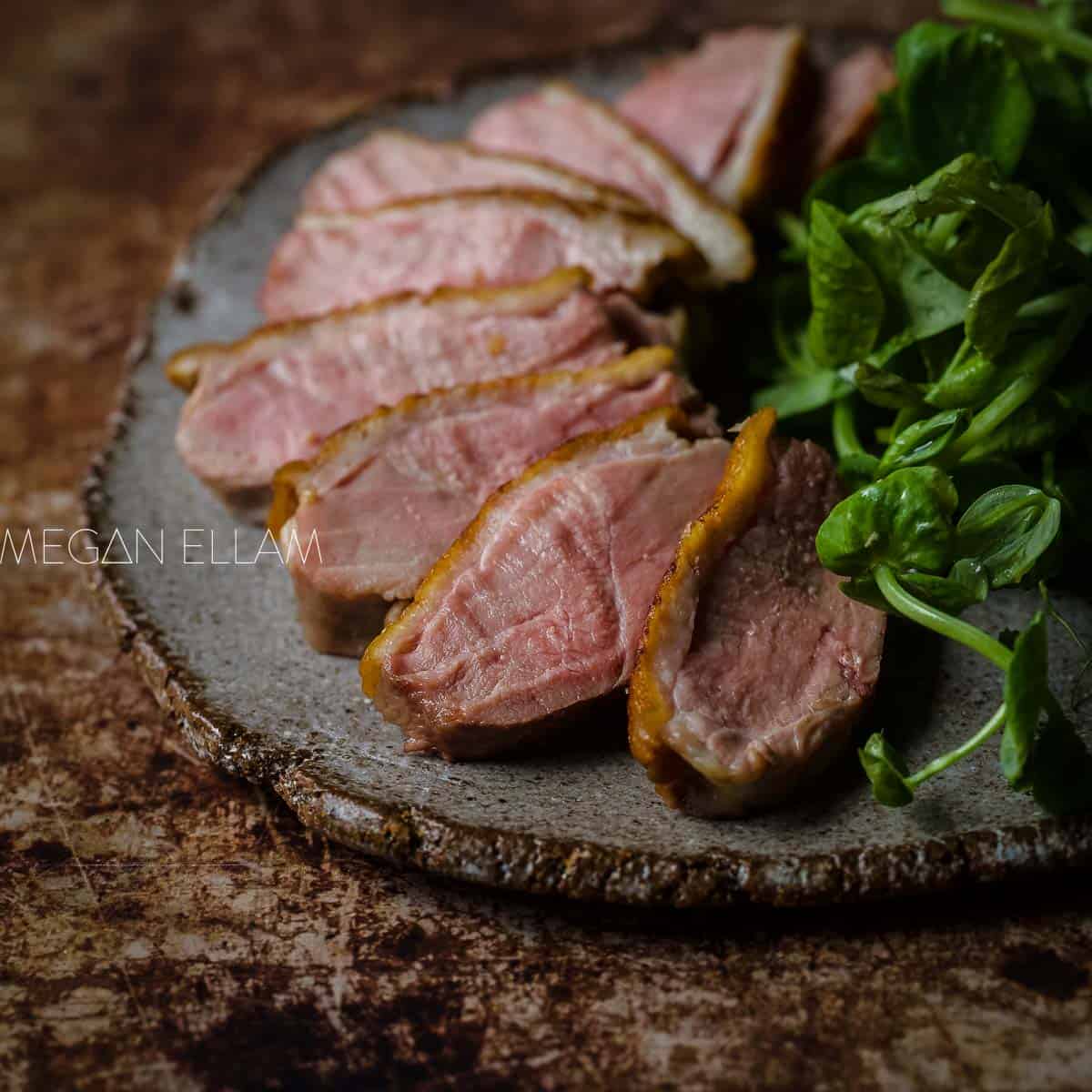 Sous Vide Duck Breast on a brown and grey plate with greens to the side.