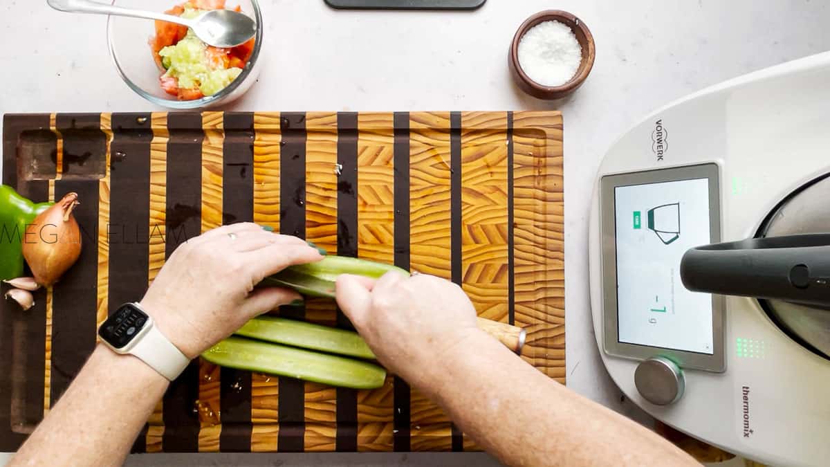 A woman slicing cucumbers on a wooden chopping board.