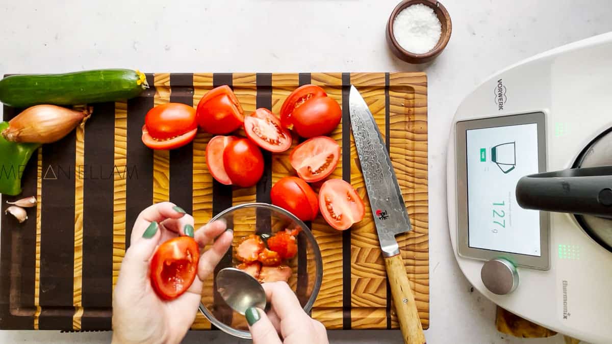 Hands deseeding a tomato into a glass bowl.