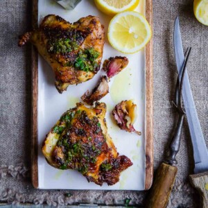 Baked Italian Chicken thighs. Overhead shot on a white platter with a sliced lemon.