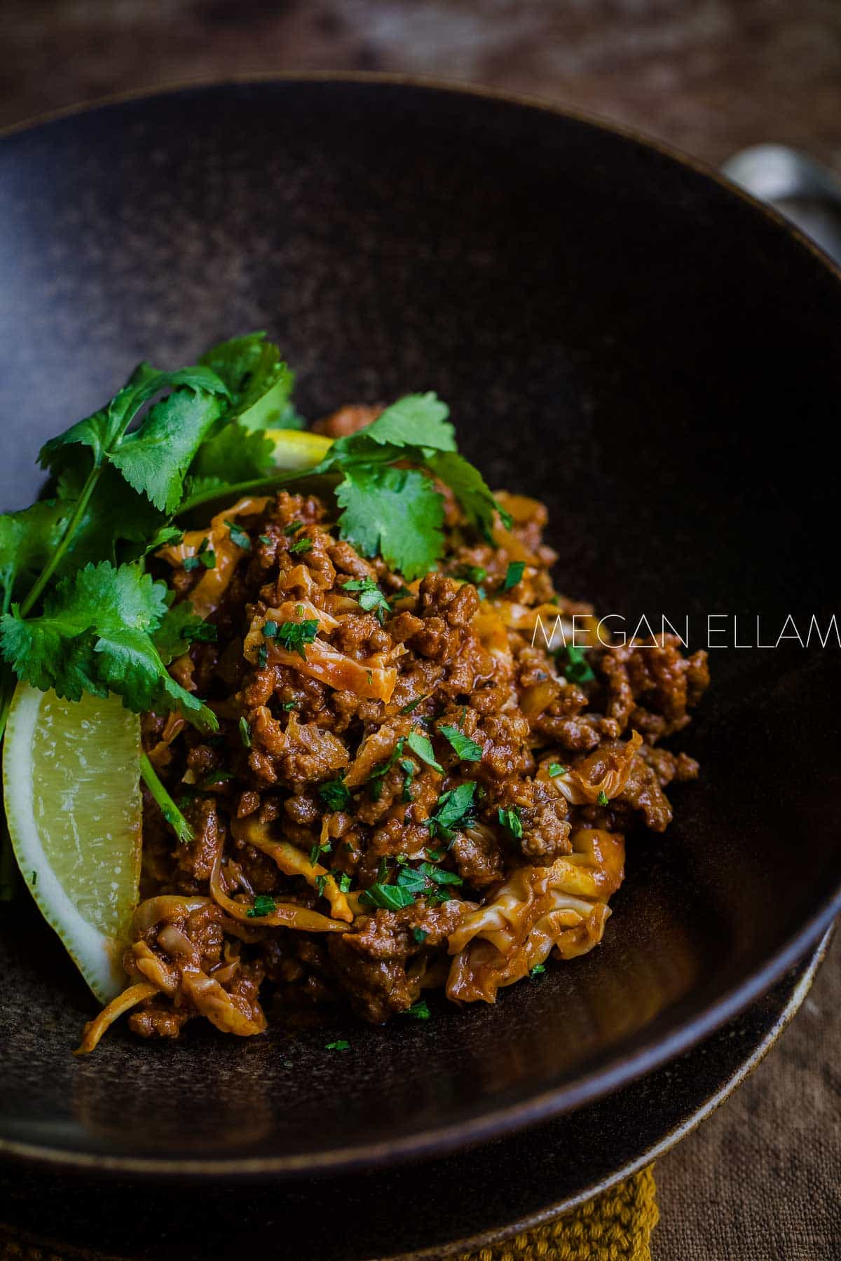 A brown bowl with beef curry in it with lemon and coriander.