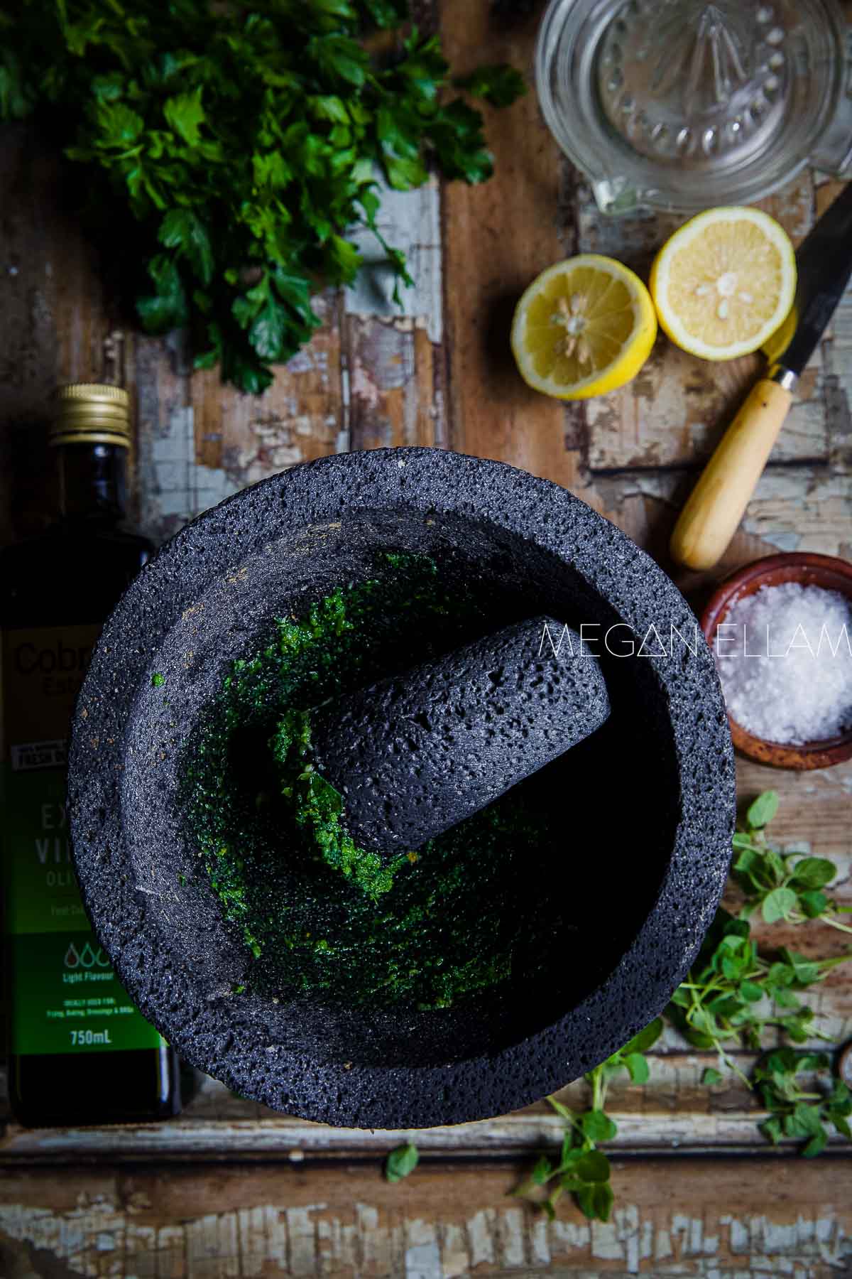 Crushed oregano and garlic in a molcajete with lemon and herbs in the background.