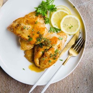 Italian Chicken Limone on a white plate with slices of lemon and fresh parsley fronds.