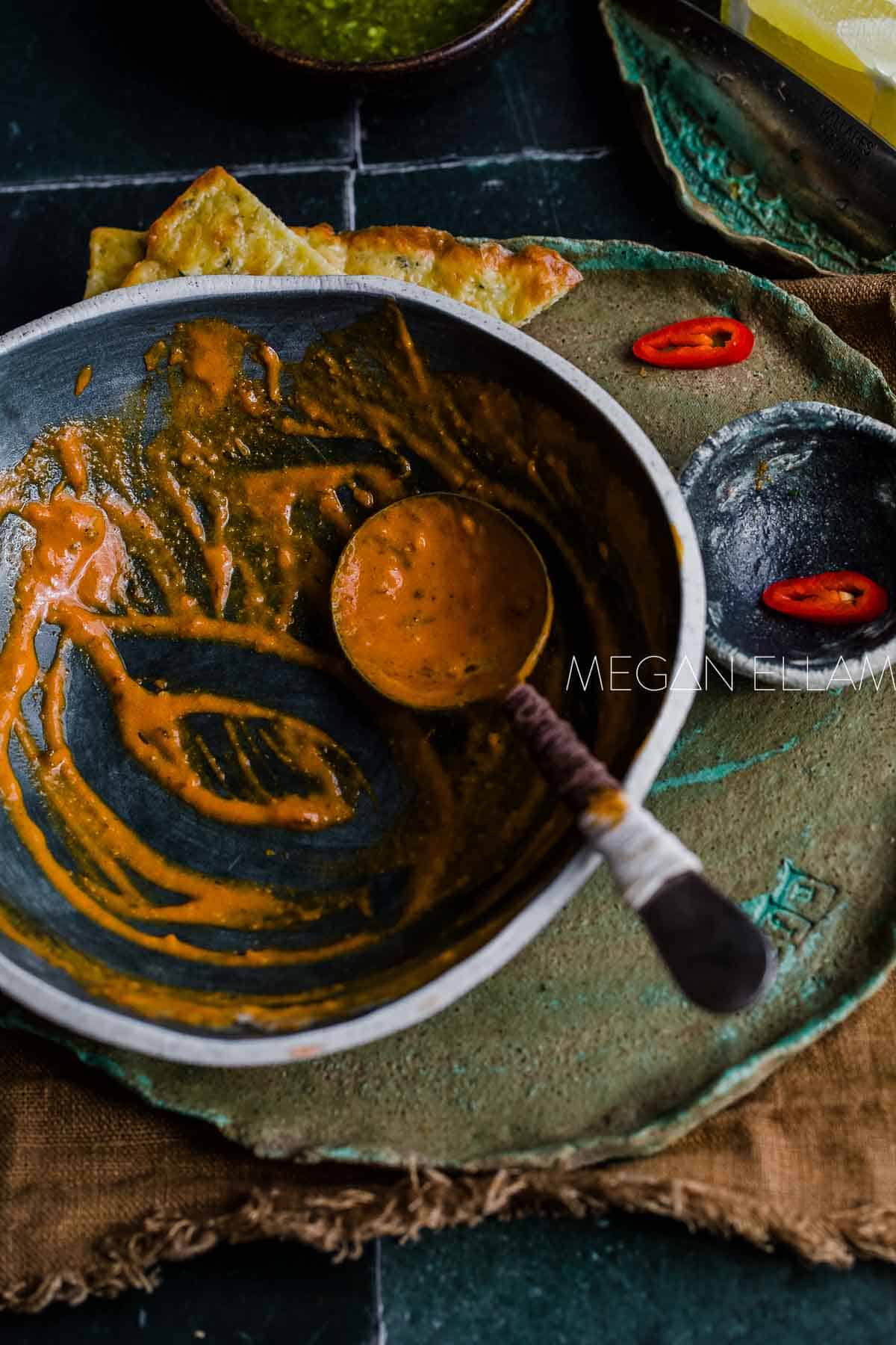An empty green bowl with masala sauce in the bottom.