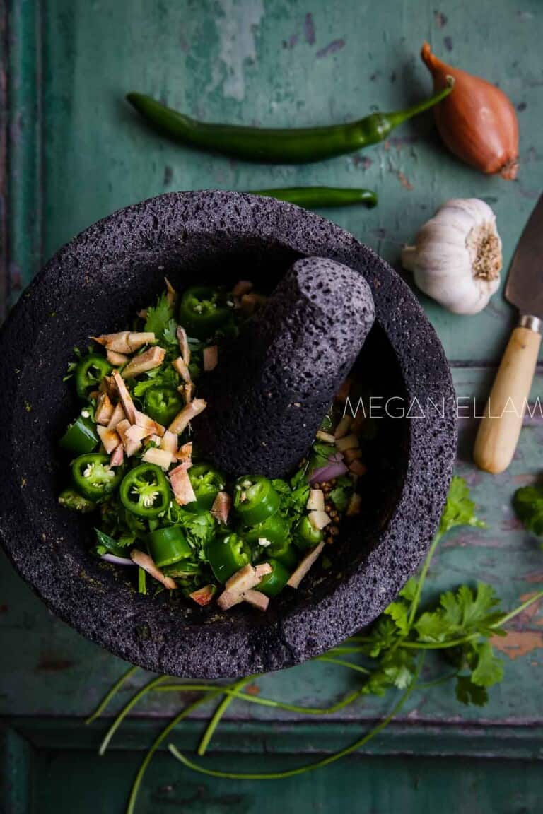 Green chilli curry paste ingredients in a black mortar and pestle.