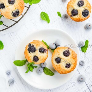 2 keto blueberry muffins on a white plate with two more muffins above to the left and right of them.