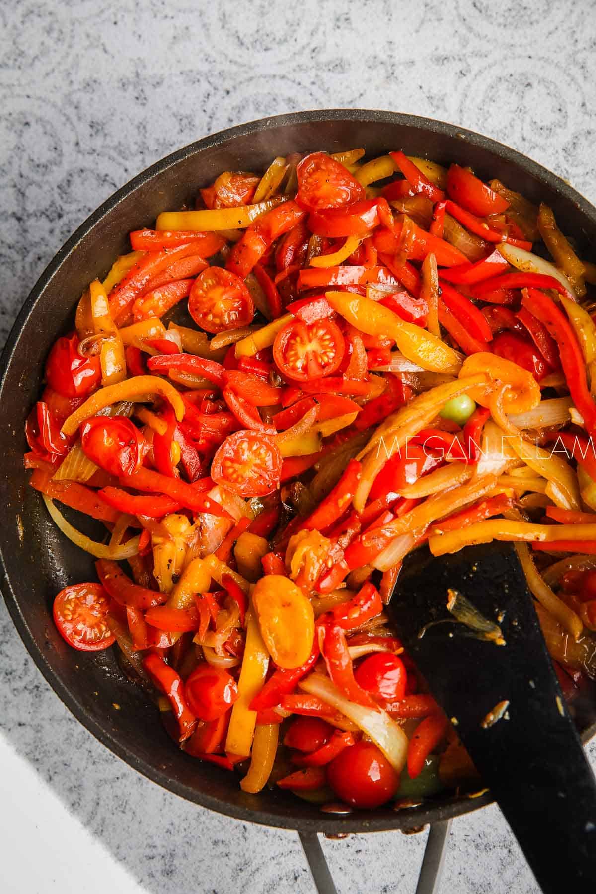 Sauteed capsicum and tomatoes inside a skillet.