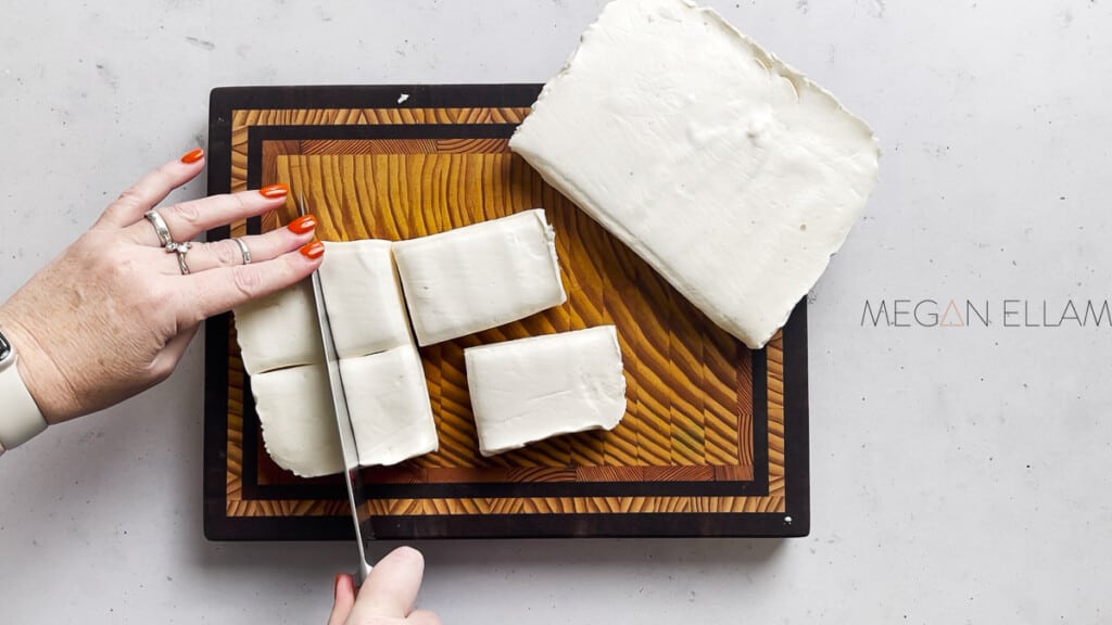 A womans hand chopping marshmallows on a chopping board.